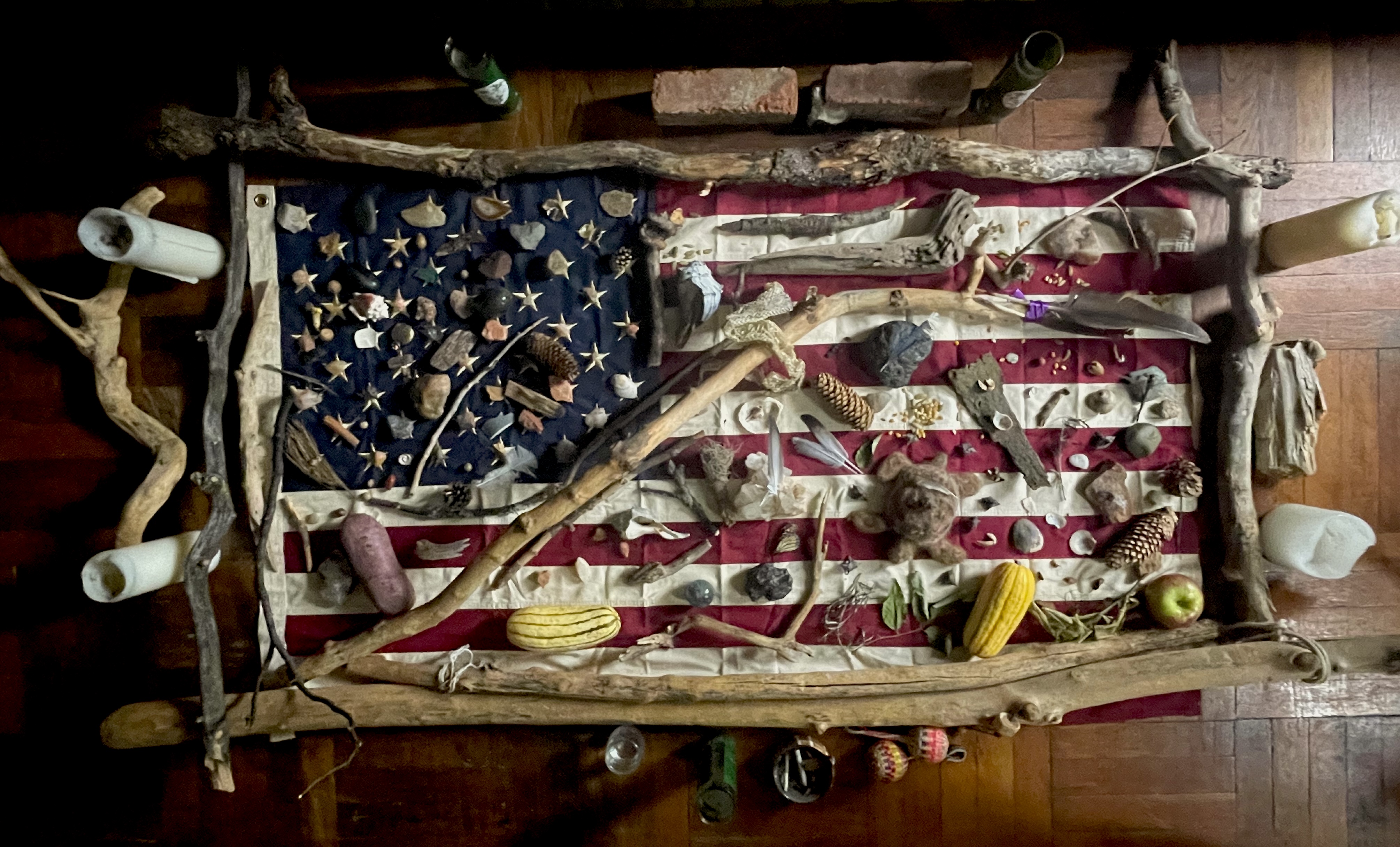 We Re/Member — flag altar installation with driftwood, stones, shells, and natural objects arranged on an American flag